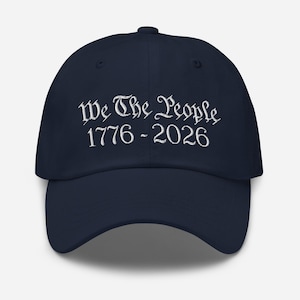 Könnte beinhalten: Marineblaue Baseballkappe mit dem gestickten Text "We The People 1776-2026" in weißer Schrift. Die Kappe hat einen gebogenen Schirm und ein klassisches Sechs-Panel-Design, ideal für den lässigen Gebrauch.