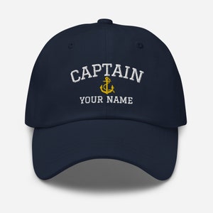 Op de afbeelding: Marineblauwe baseballcap met wit geborduurde tekst "CAPTAIN" boven "YOUR NAME" en een gouden ankerembleem. Een klassieke pet voor liefhebbers van de zeevaart.