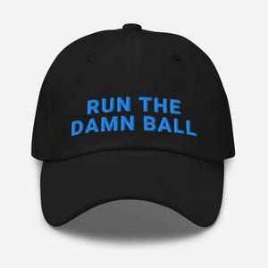 May include: Black baseball cap with blue embroidered text that reads "RUN THE DAMN BALL".