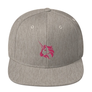 Puede incluir: Una gorra de béisbol gris y gris jaspeado con una cabeza de unicornio bordada en rosa en la parte delantera.