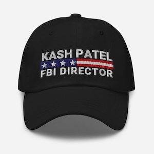 Könnte beinhalten: Schwarze Baseballkappe mit gesticktem Text "KASH PATEL FBI DIRECTOR" über einer stilisierten amerikanischen Flagge. Die Kappe hat einen gebogenen Schirm und einen verstellbaren Riemen hinten.
