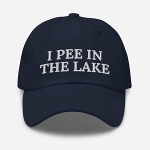 May include: A navy blue baseball cap with white embroidered text that reads "I PEE IN THE LAKE".