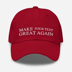 Peut inclure: Casquette de baseball rouge avec un texte brodé en blanc qui dit "MAKE YOUR TEXT GREAT AGAIN".