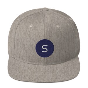 Puede incluir: Una gorra de béisbol de visera plana gris y azul con un círculo azul marino y una letra "S" blanca en el centro.