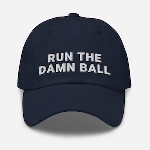 May include: A navy blue baseball cap with white embroidered text that reads "RUN THE DAMN BALL".