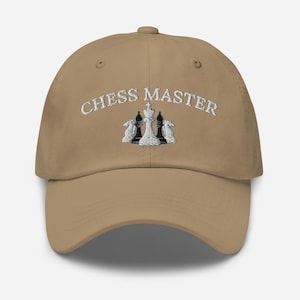 Puede incluir: Una gorra de béisbol de color caqui con el texto "Chess Master" bordado en blanco en la parte delantera. Un diseño de piezas de ajedrez blancas y negras está bordado debajo del texto.