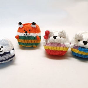 Puede incluir: Cuatro animales de peluche tejidos, incluyendo un zorro y tres osos. El zorro es naranja y verde con ojos negros. Los osos son blancos con ojos negros y rayas de diferentes colores. El primer oso tiene rayas azules y blancas, el segundo tiene rayas rojas, amarillas y moradas, y el tercero tiene rayas azules, amarillas y moradas con una corbata de lazo azul.