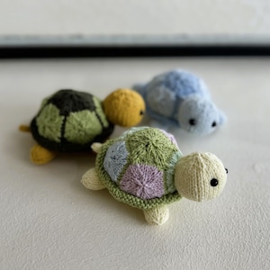 May include: Three knitted turtle toys. One is green and brown, one is light blue, and one is light green and pink with a yellow head.