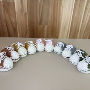 以下が含まれることがあります： マスタードイエロー、ピンク、グレー、グリーンなど、さまざまな色のニット製のベビーブーティ9足セット。各ブーティには白いつま先と白いレースアップのディテールがあります。