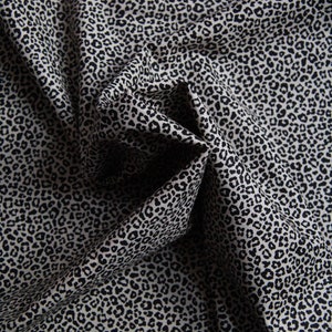 Peut inclure: Gros plan sur un tissu à motif léopard. Le tissu est de couleur beige clair avec des taches noires de tailles variables. Le tissu est plié et drapé, créant des ombres et de la texture.