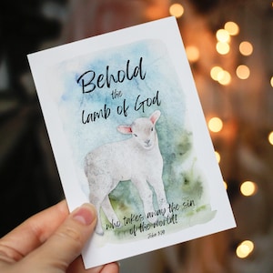 Könnte beinhalten: Weiße Karte mit einer Aquarellillustration eines Lammes und dem Text "Seht, das Lamm Gottes, das die Sünde der Welt hinwegnimmt! Johannes 1,29". Der Hintergrund zeigt blaue und grüne Aquarellwaschungen.