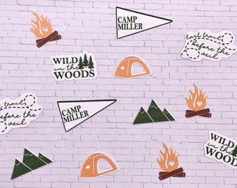 May include: A collection of camping themed stickers featuring a tent, mountains, a campfire, and the text "WILD in the WOODS" and "CAMP MILLER".