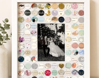 May include: A white rectangular picture frame containing a central black and white photograph of a couple in wedding attire, surrounded by a border of small, circular paper cutouts featuring various patterns, colors, and wedding-themed text.