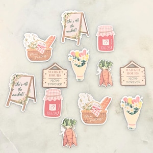 May include: A collection of stickers featuring a market theme. Designs include signs that read "She's off the market!" and "Market Hours Now-Forever", bouquets of flowers, carrots, jam jars, and baskets of flowers and bread.