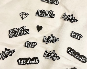 May include: A selection of black and white die-cut shapes on a white background. The shapes feature phrases such as "Bye Bye Beauman", "Bride or Die", "RIP", and "Till Death", alongside a diamond and a heart.