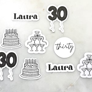May include: A selection of black and white stickers with a birthday theme. Designs include the number 30 as balloons, a tiered cake with candles, champagne glasses, the name "Laura", and the word "thirty".