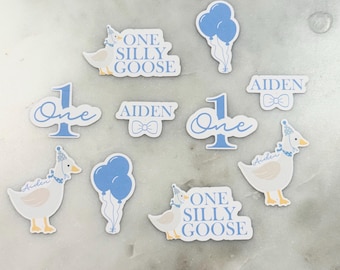 May include: A set of nine blue and white stickers featuring a goose with a party hat and the text "One Silly Goose". The stickers also include the number one, the name Aiden, and a bow tie.