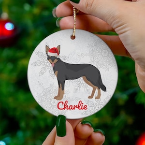 May include: A round, white Christmas ornament featuring a cartoon dog wearing a Santa hat and sunglasses, with the name "Charlie" in red. The ornament has a gold string for hanging and a snowflake background.