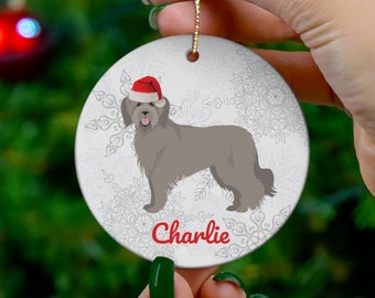 May include: A round Christmas ornament featuring a gray dog wearing a Santa hat, with the name "Charlie" in red script. The ornament has a snowflake background and a gold string for hanging.