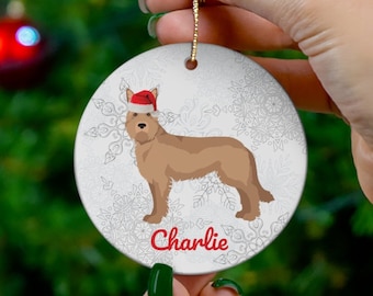 May include: A round Christmas ornament featuring a brown dog wearing a Santa hat, with the name "Charlie" in red. The ornament has a snowflake pattern on a white background and a gold string for hanging.