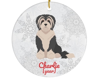 May include: A white ceramic Christmas ornament with a black and white dog illustration. The dog is sitting and has a snowflake pattern background. The ornament has the text "Charlie [year]" in red.