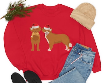 Könnte beinhalten: Rotes Sweatshirt mit zwei Cartoon-Hunden, die Weihnachtsmützen tragen. Ein Hund hält einen Fisch. Eine beige Mütze, blaue Jeans und schwarze Schuhe sind ebenfalls zu sehen. Ein Zweig mit Grünzeug sorgt für eine festliche Note.