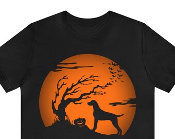 May include: A black short-sleeve t-shirt featuring a graphic print of a large orange full moon. The design includes a black silhouette of a dog standing next to a jack-o'-lantern and a bare tree, with a flock of bats flying across the moon.