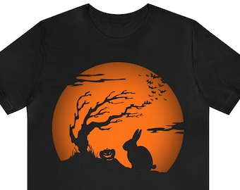 Könnte beinhalten: Schwarzes T-Shirt mit einem Halloween-Motiv. Die Grafik zeigt einen Hasen, einen Baum und einen geschnitzten Kürbis vor einem orangefarbenen Vollmond. Fledermäuse fliegen am Himmel. Das Design ist auf ein schwarzes T-Shirt gedruckt.