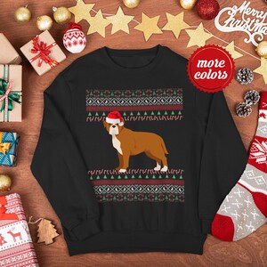 May include: Black Christmas sweater with a red and white pattern. A brown and white dog wearing a Santa hat is in the center of the sweater.