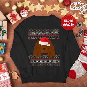 May include: Black Christmas sweater with a red and white holiday pattern. A brown and white dog wearing a red Santa hat is in the center of the sweater.