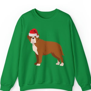 May include: A green sweatshirt featuring a brown dog wearing a red and white Santa hat. The dog has white markings on its chest and paws. The sweatshirt is a solid green color.