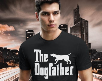 Può includere: Una maglietta nera con una grafica bianca che dice "The Dogfather" e presenta una silhouette bianca di un cane che corre.