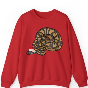 Op de afbeelding: Een rode sweatshirt met een cartoon slang met een kerstmuts. De slang is bruin, bruin en zwart, met een rode tong. De kerstmuts is rood en wit. De sweatshirt heeft lange mouwen.