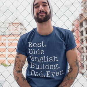 May include: A man wearing a blue t-shirt with white text that reads "Best Olde English Bulldog Dad Ever".