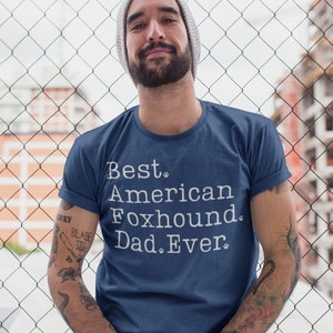 May include: A navy blue t-shirt with white text that reads "Best American Foxhound Dad Ever" with paw prints.