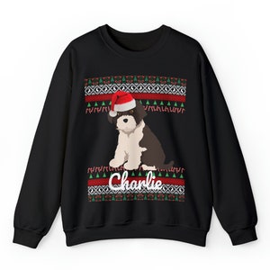 May include: Black Christmas sweater with a white dog wearing a Santa hat. The sweater has a red and green pattern with the name "Charlie" written on it.