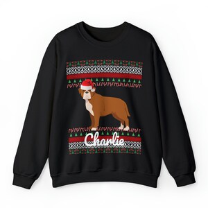 May include: Black Christmas sweater with a red and green pattern. A brown and white dog wearing a Santa hat is in the center of the sweater. The text "Charlie" is below the dog.