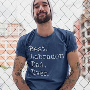 May include: A man wearing a blue t-shirt with the text "Best Labrador Dad Ever" in white with paw prints.