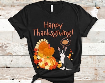 Puede incluir: Camiseta negra con temática de Acción de Gracias. La camiseta presenta el texto "Happy Thanksgiving!" en naranja, junto con ilustraciones de un pavo, calabazas, hojas de otoño y un perro Boston Terrier. El perro tiene una burbuja de pensamiento con una pata de pavo.