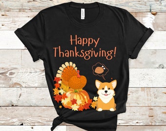 Op de afbeelding: Zwart T-shirt met een Thanksgiving-thema. De oranje tekst luidt "Happy Thanksgiving!". Het shirt heeft ook een kalkoen, pompoenen, herfstbladeren en een cartoon corgi-hond.