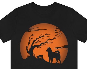 May include: A black short-sleeve t-shirt featuring a graphic print of a dog standing next to a jack-o'-lantern and a bare tree against a large orange full moon. The scene includes silhouettes of flying bats in the upper right corner.
