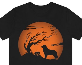 Puede incluir: Una camiseta negra de manga corta con un estampado gráfico de un perro de pie junto a una calabaza y un árbol desnudo frente a una gran luna naranja circular. El diseño incluye siluetas de murciélagos volando y nubes dentro de la luna.