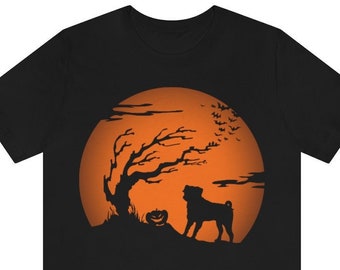 Puede incluir: Una camiseta negra de manga corta con un estampado gráfico de la silueta de un perro de pie junto a una calabaza de Halloween y un árbol desnudo frente a una gran luna naranja circular con murciélagos volando al fondo.