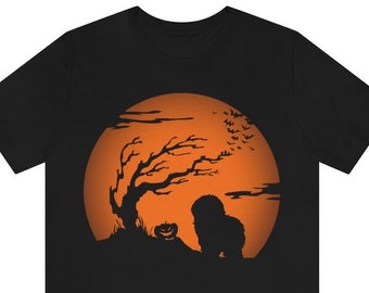 May include: A black short-sleeved t-shirt featuring a graphic print of a large orange full moon. The design includes a silhouette of a bare tree, a carved jack-o'-lantern pumpkin, a small dog, and a flock of bats flying across the moon's surface.
