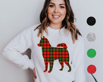 Puede incluir: Sudadera blanca con una silueta de perro a cuadros en rojo, verde y marrón. El diseño del perro es un patrón de cuadros festivo. La sudadera tiene cuello redondo y mangas largas. La imagen también muestra muestras de color.