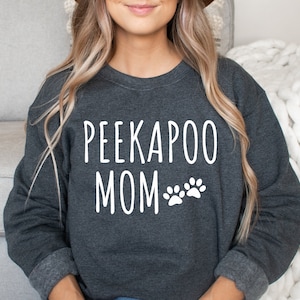 Può includere: Una felpa grigia scura con il testo "PEEKAPOO MOM" e due impronte di zampa bianche.