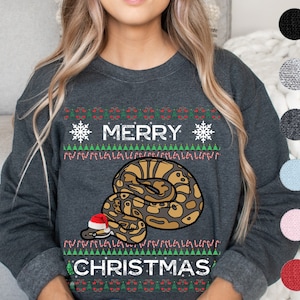 Op de afbeelding: Een donkergrijs sweatshirt met een kerstthema met een slang die een kerstmanmuts draagt en de woorden "Merry Christmas".