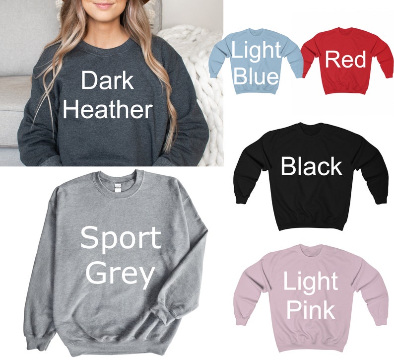 May include: A selection of crewneck sweatshirts in various colors, including dark heather, light blue, red, black, sport grey, and light pink. Each sweatshirt has the color name printed in white on the front. The sweatshirts are made of a soft material.