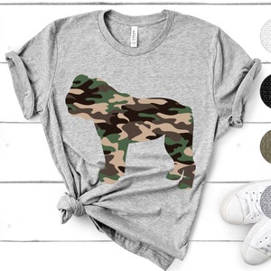 May include: A gray t-shirt with a camouflage pattern gorilla silhouette on the front. The t-shirt is made of a soft, comfortable material and is perfect for everyday wear.