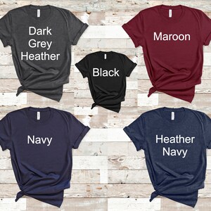 May include: Five t-shirts in different colors: dark grey heather, black, maroon, navy, and heather navy. Each shirt has a white text label with the color name.